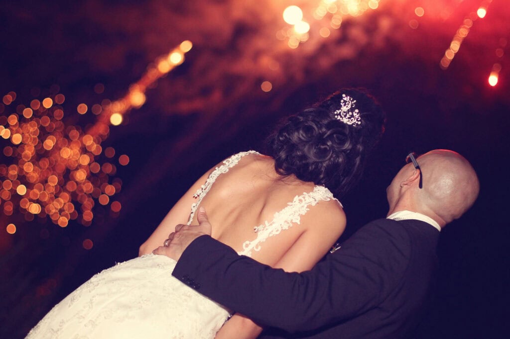 Nighttime wedding fireworks: make your big day go off with a bang! 🎆 2 Wedding couple watching fireworks at night, bride in white dress.