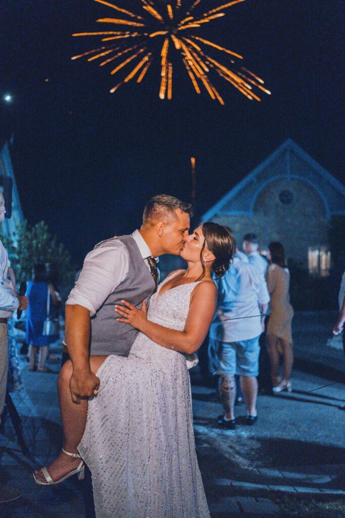 Nighttime wedding fireworks: make your big day go off with a bang! 🎆 1 Wedding couple kissing at a night event, with fireworks in the background.