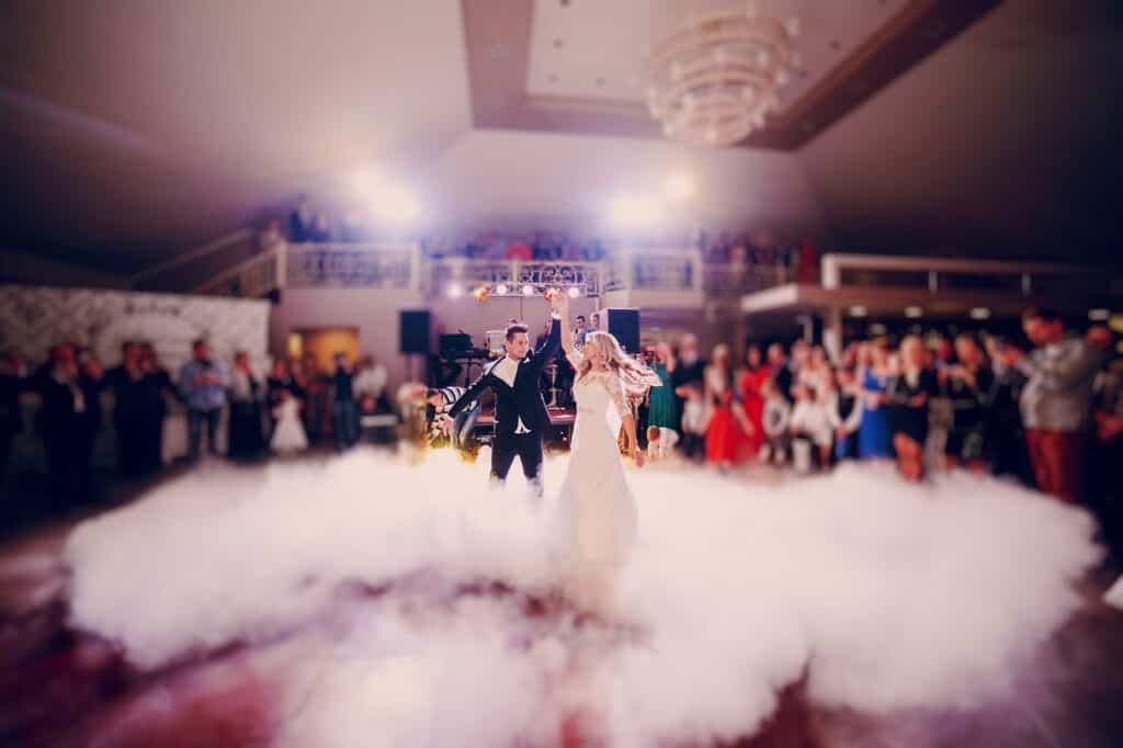 Wedding first dance: 10 things you need to know about your wedding first dance! 💃🕺 2 wedding opening dance - Wedding couple dancing indoors at a reception with thick smoke, guests around them.