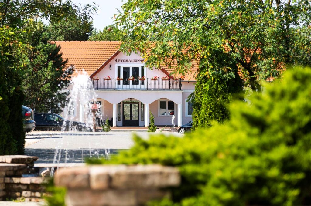 Bodrogi Kúria - Pygmalion - Épület "Pygmalion" felirattal, szökőkút és növények előtérben, zöldellő környezet.