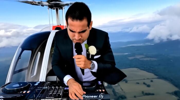 esküvői dj és ceremóniamester - Férfi öltönyben helikopter tetején DJ-felszereléssel zenél, körülötte kék ég és felhők.